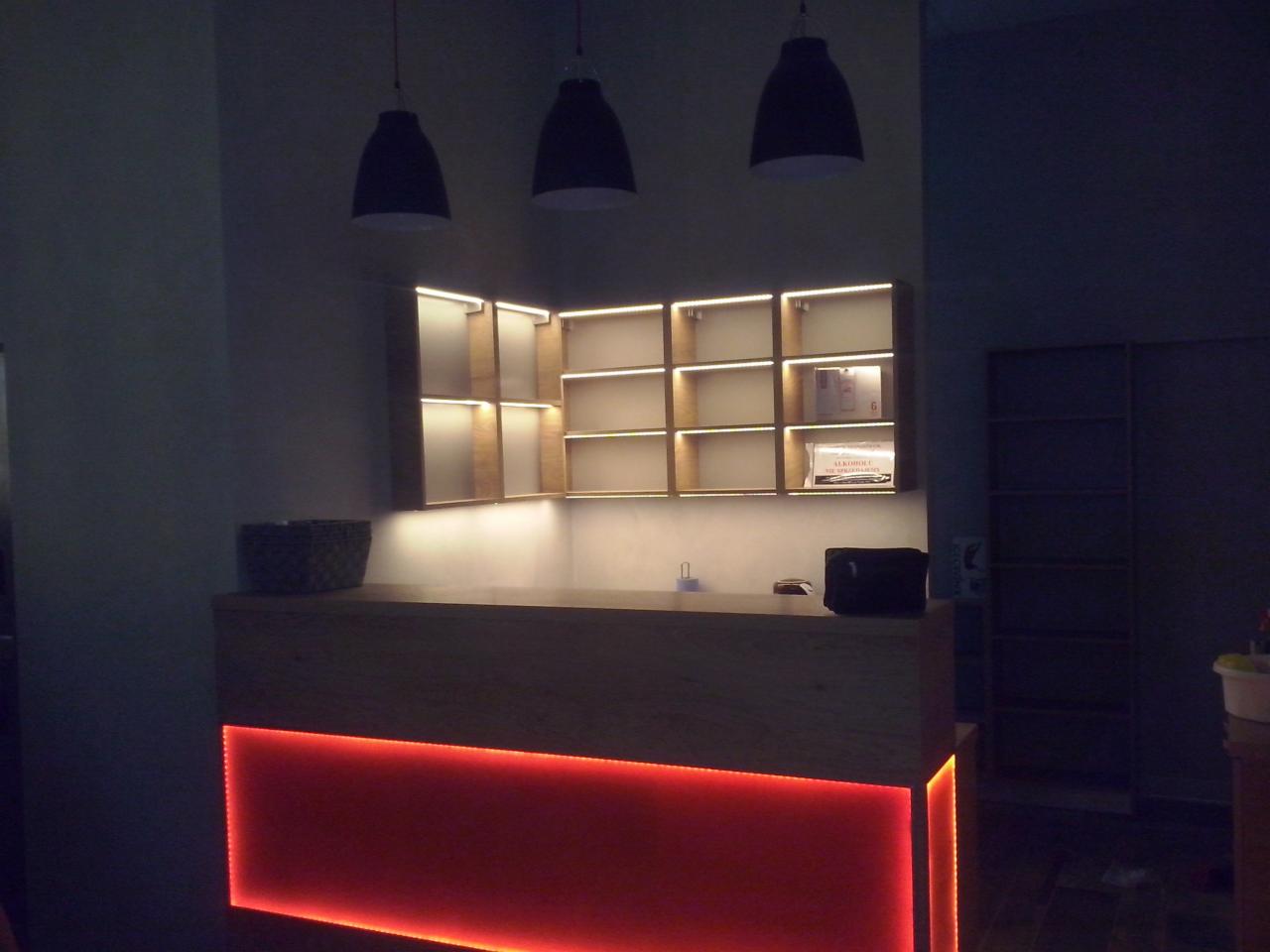 Nowoczesne wykończenie wnętrza: drewniana lada z czerwonym podświetleniem LED, półki z oświetleniem i wiszące lampy. Minimalistyczny design w ciemnym pomieszczeniu.