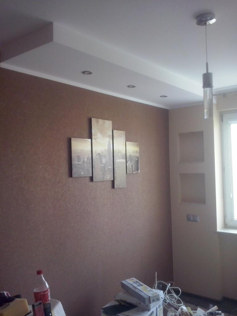Pokój po remoncie: brązowa ściana z obrazami, podwieszany biały sufit z oświetleniem punktowym, wisząca lampa. Na podłodze akcesoria remontowe.