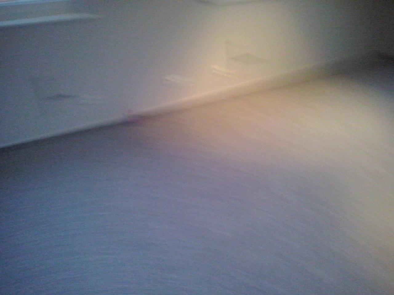 Rozmyte ujęcie gładkiej, pomalowanej ściany w odcieniach szarości i bieli, z delikatnym załamaniem światła w górnym rogu. Tekstura ściany jest ledwo widoczna.