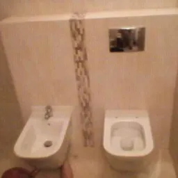 Wykończona łazienka w beżowych tonacjach: wisząca toaleta i bidet z baterią, oddzielone pionowym pasem mozaiki. Na ścianie chromowany przycisk spłuczki.