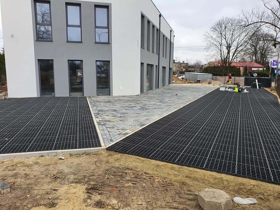 Prace brukarskie w Łodzi: Połączenie kostki brukowej i ażurowych płyt na podbudowie, widoczne prace wykończeniowe przy budynku.