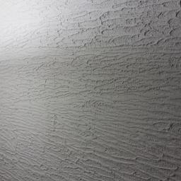 Loukas - Szara ściana z dekoracyjnym, strukturalnym tynkiem w stylu baranka, oświetlona od góry, z widoczną fakturą i cieniem.