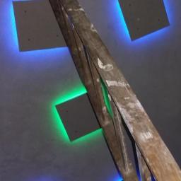 Loukas - Sufit podwieszany z kwadratowymi panelami LED w kolorach niebieskim i zielonym, z drewnianą drabiną opartą o ścianę. Ujęcie z dołu, pod kątem.