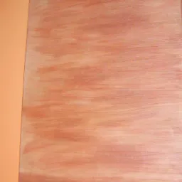 Fragment ściany z efektem dekoracyjnym imitującym drewno, obok pomarańczowa ściana. Delikatne, poziome smugi w odcieniach brązu nadają wnętrzu ciepły charakter.