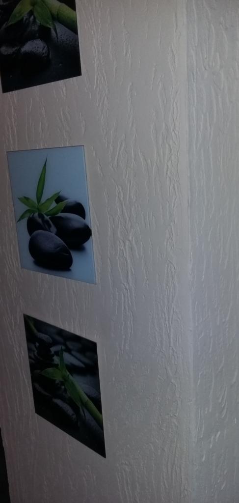 Ściana z fakturą i trzy kwadratowe obrazy z motywem kamieni zen i bambusa, ułożone pionowo. Obrazy mają różne kąty nachylenia.