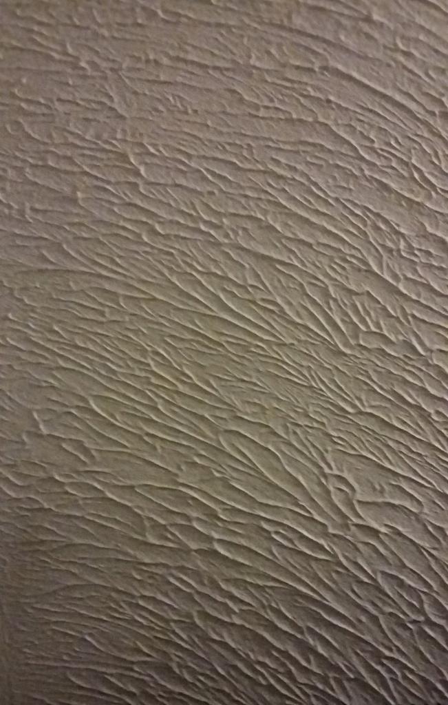 Szara ściana z wyraźną fakturą w ukośne wzory, przypominająca płynącą wodę. Delikatne cieniowanie podkreśla trójwymiarowość wzoru.