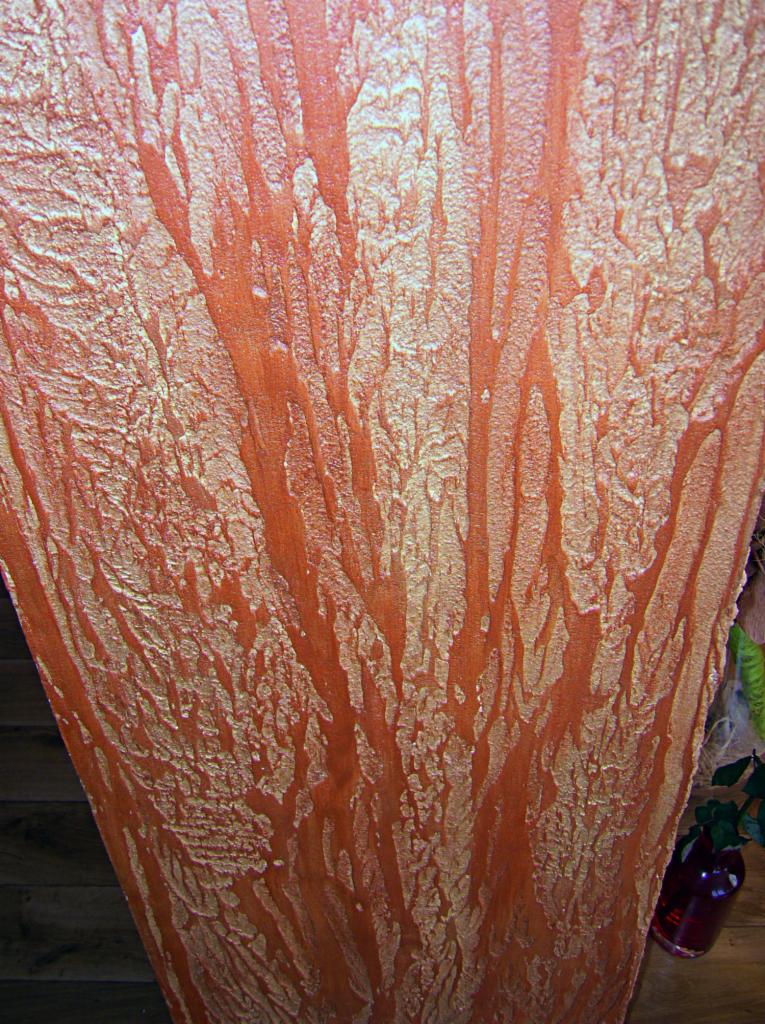 Dekoracyjna ściana w odcieniach pomarańczy i złota z unikalną teksturą imitującą korę drzewa. Widoczne nieregularne wzory i subtelne refleksy świetlne.