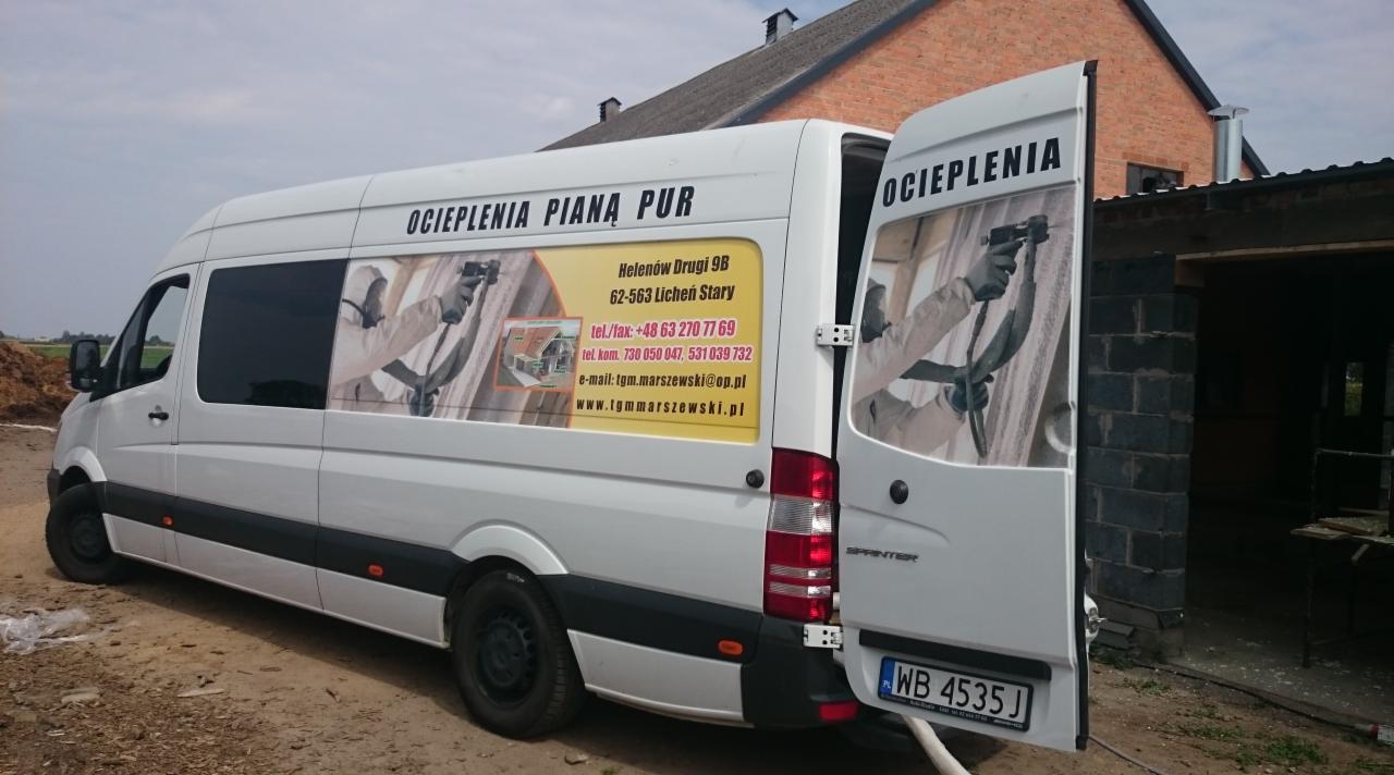 Biały samochód dostawczy z reklamą firmy ociepleniowej, widoczny adres i dane kontaktowe na karoserii, otwarte tylne drzwi ukazują wnętrze budynku w tle.