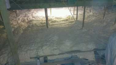 Izolacja poddasza wykonana metodą natrysku, widoczne równomierne pokrycie materiałem termoizolacyjnym pomiędzy elementami konstrukcji drewnianej dachu, oświetlone punktowo