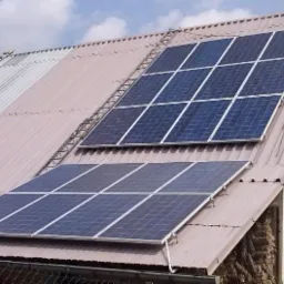 Dwa panele słoneczne, każdy z dziewięcioma ogniwami, zamontowane na blaszanym dachu budynku gospodarczego w słoneczny dzień.