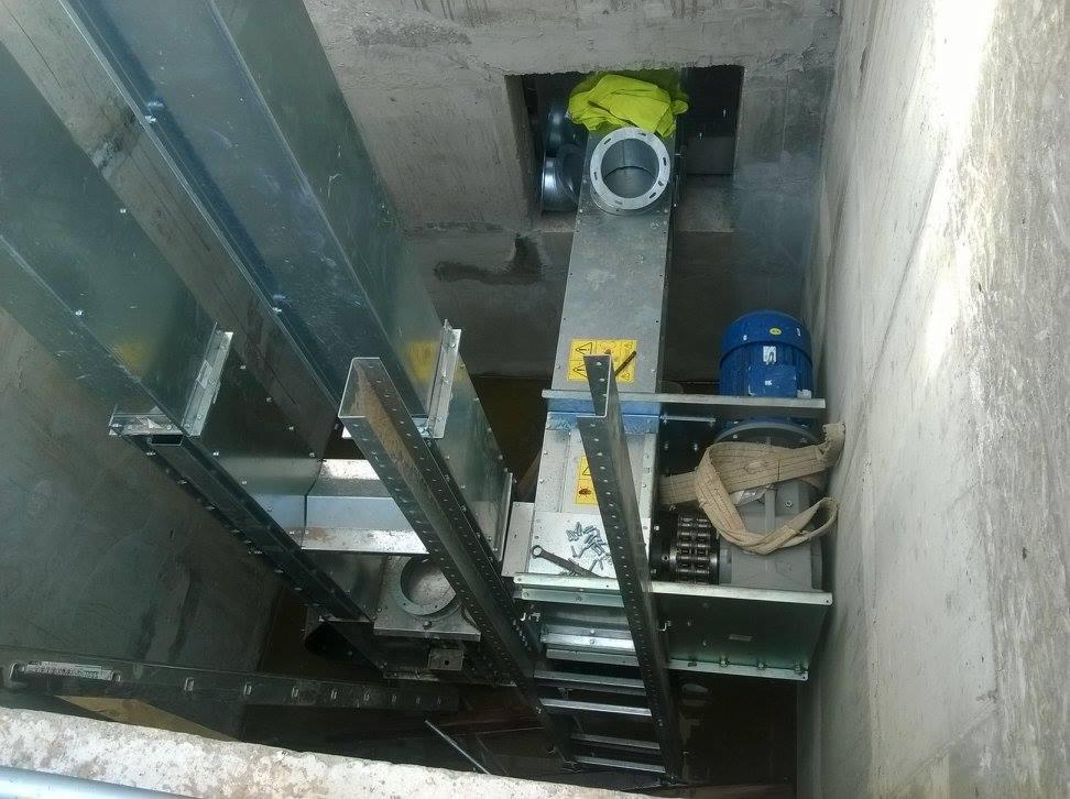 Wnętrze hali z elementami konstrukcji stalowej: profile, łączenia, silnik. Widok z dołu na metalowe komponenty i betonowe ściany. Żółta tkanina w tle.