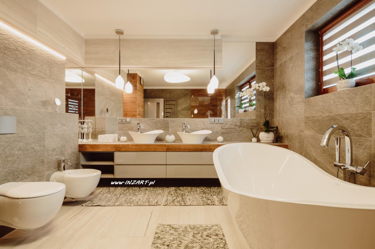 Nowoczesna łazienka z wolnostojącą wanną, dwoma umywalkami nablatowymi, bidetem i toaletą w odcieniach szarości z akcentami drewna i roślinami w oknie.