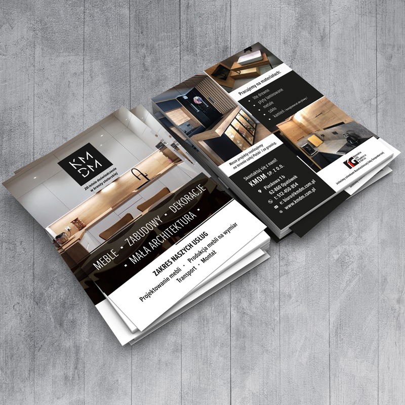 Stos ulotek reklamowych firmy KMDM prezentujących meble na wymiar, zabudowy i dekoracje, z widocznymi zdjęciami realizacji kuchni i łazienki.