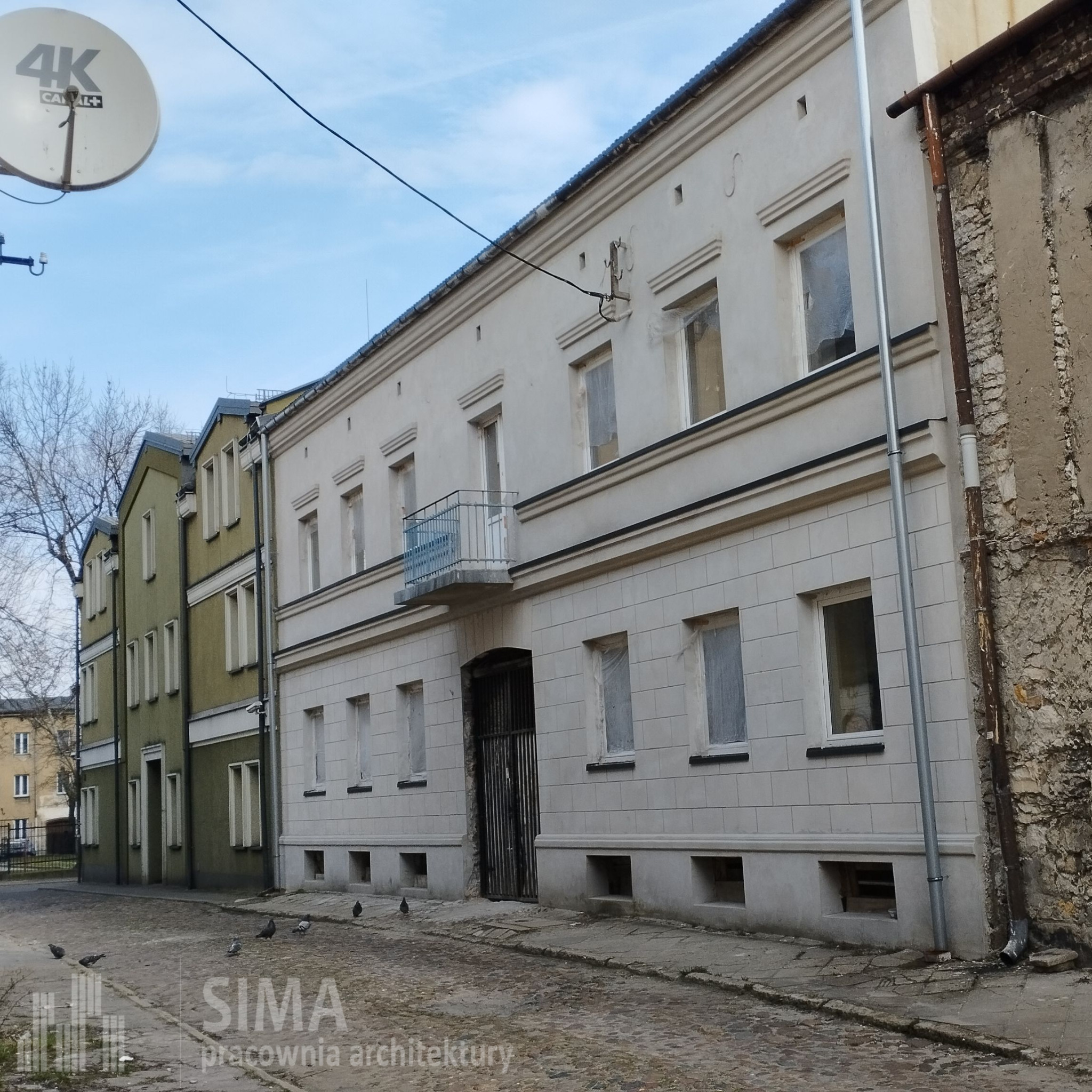 Kamienica w Częstochowie w trakcie remontu elewacji, z oknami zabezpieczonymi folią, widoczna z poziomu ulicy wyłożonej kostką brukową, z gołębiami na pierwszym planie i anteną satelitarną na dachu.