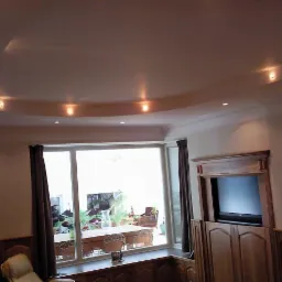 Elegancki salon z podwieszanym sufitem z wbudowanym oświetleniem punktowym. Widoczne okno z widokiem na taras i drewniane meble.