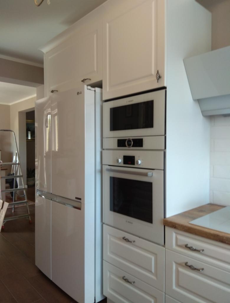 Biała kuchnia z zabudową, piekarnikiem i mikrofalówką Bosch oraz lodówką LG, widok z boku na jasne drewniane podłogi.