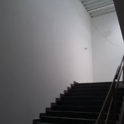 Świeżo otynkowana ściana cm-wap na klatce schodowej, zacierana pod malowanie, widoczne schody i fragment drewnianej barierki.