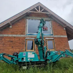 Montaż okna w surowym domu z cegły za pomocą specjalistycznego dźwigu, widok z dołu. Dom w trakcie budowy, okna z ramami w kolorze drewna.