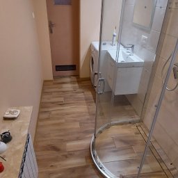 Remont BEST-EVER Usługi remontowo budowlane Konrad Oleksiak - Nowoczesna łazienka z kabiną prysznicową typu walk-in, umywalką z szafką, pralką i grzejnikiem, wykończona płytkami imitującymi drewno.