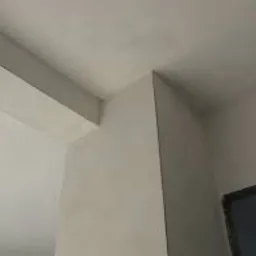 Wykończony narożnik ścian i sufitu, świeżo pomalowany na jasny odcień szarości, widoczne lekkie niedoskonałości faktury powierzchni, kadr od dołu.