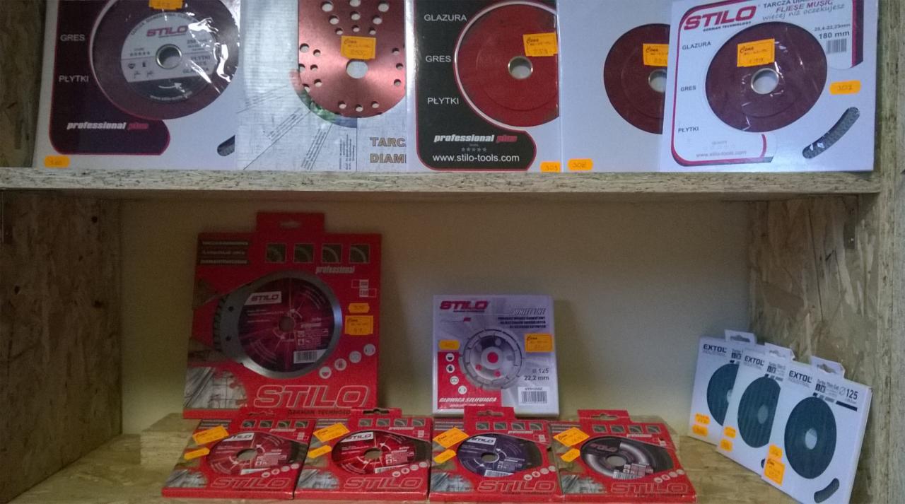 Ekspozycja tarcz diamentowych Stilo i Extol do cięcia glazury, gresu i płytek, ułożonych na drewnianej półce w sklepie. Widoczne ceny na opakowaniach.