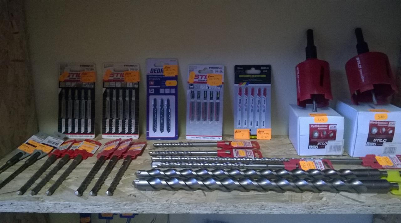 Różne wiertła i otwornice Stilo na półce, w opakowaniach i luzem, z cenami. Widoczne wiertła do betonu, metalu i drewna. Produkty DEDRA i STILO.