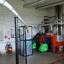 Kompleksowa kotłownia z piecem na paliwo stałe, instalacją rur, panelem sterowania i narzędziami. Widoczne elementy zabezpieczeń ppoż. i wentylacja.