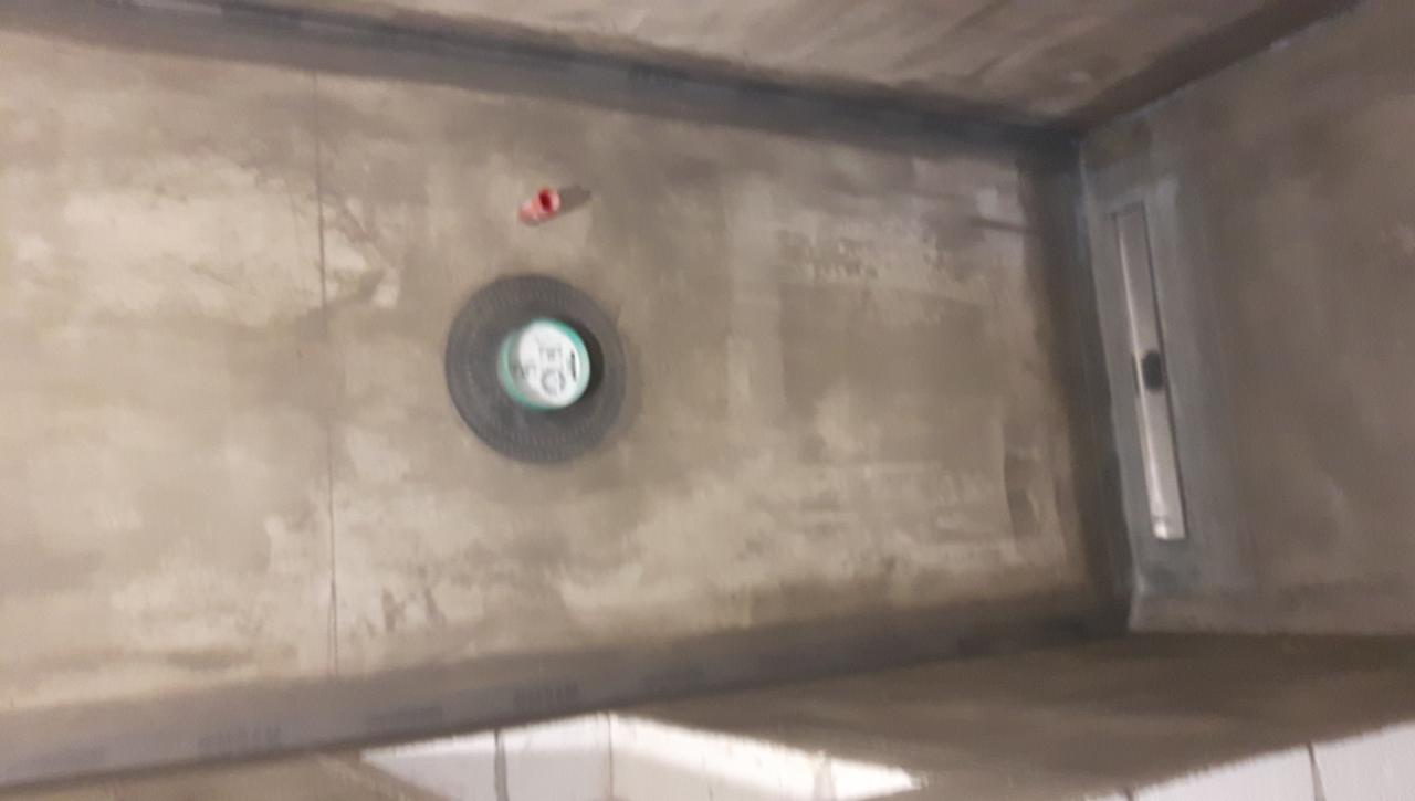 Przygotowana do wykończenia posadzka z odpływem liniowym i centralnym, widoczne elementy instalacji wodnej.