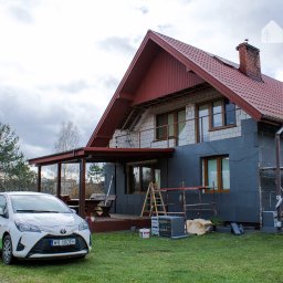 WOJTMAR - Dajemy Energię! - Dom jednorodzinny w trakcie ocieplania grafitowym styropianem, widoczne rusztowania, drabina i materiały budowlane, na pierwszym planie samochód firmowy z logo.
