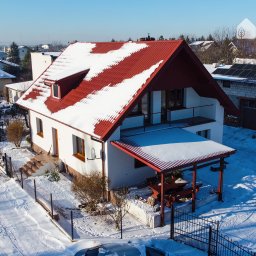 WOJTMAR - Dajemy Energię! - Dom jednorodzinny z czerwoną dachówką częściowo pokrytą śniegiem, panele słoneczne na budynku gospodarczym w tle, zimowy krajobraz.