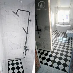 Wykończona łazienka z marmurowymi ścianami, czarno-białą szachownicą na podłodze, nowoczesną kabiną prysznicową z czarną armaturą oraz wolnostojącą wanną i toaletą. Widoczne niedokończone kable...