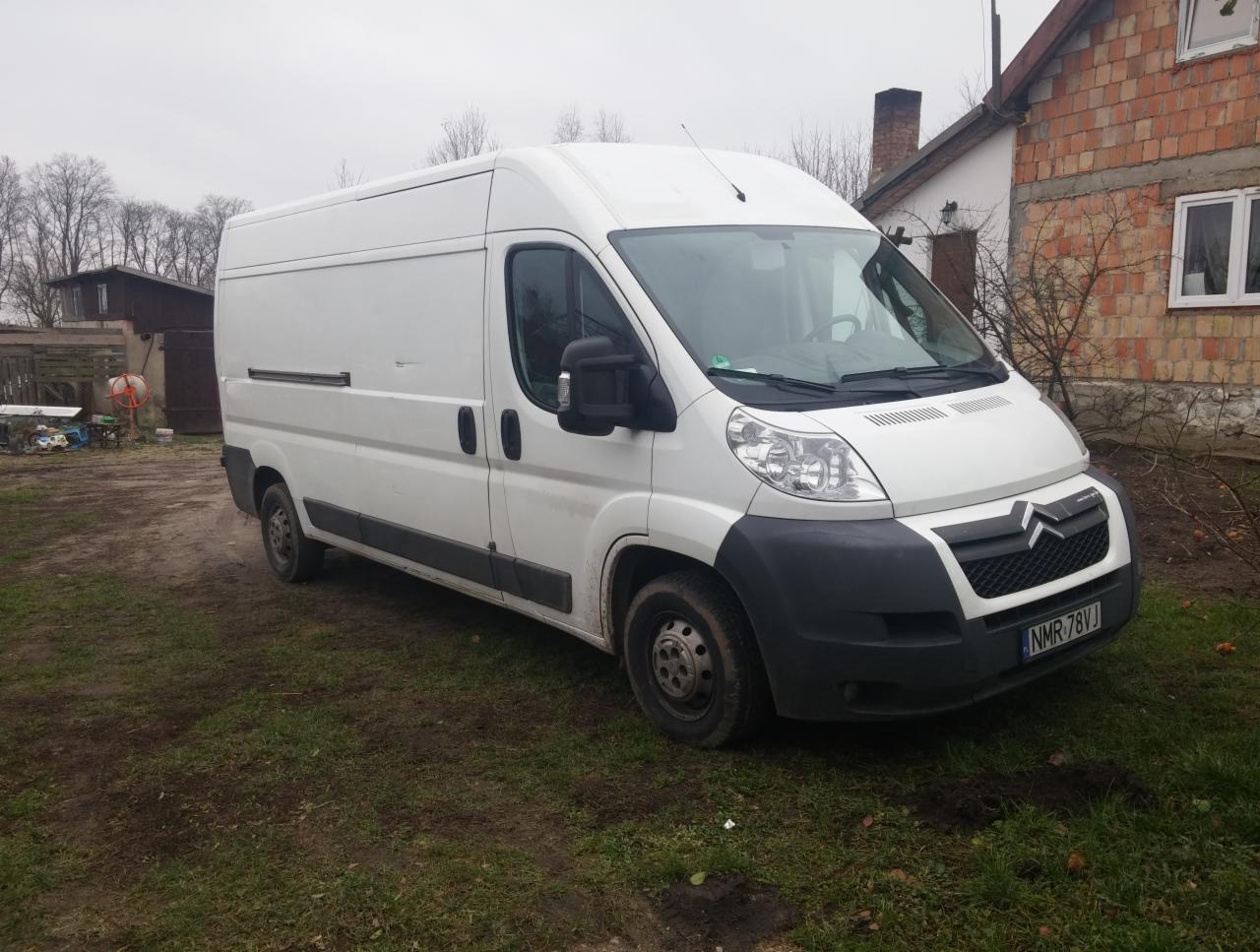 Biały Citroen Jumper, bus dostawczy na trawiastym terenie, widok z przodu, szary dzień. Widoczne zabudowania w tle. Tablica rejestracyjna NMR 78VJ.