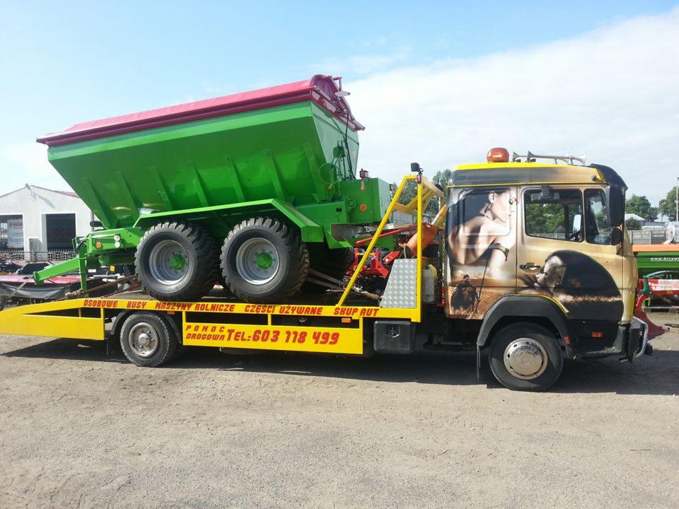 Żółta laweta z zielonym rozsiewaczem na naczepie. Laweta ma grafiki na kabinie i napis 'Pomoc Drogowa Tel: 603 118 499'.