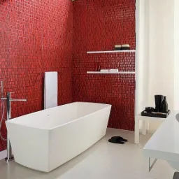 Nowoczesna łazienka z wanną wolnostojącą i ścianą wyłożoną czerwoną mozaiką, uzupełniona białymi półkami i minimalistyczną armaturą.