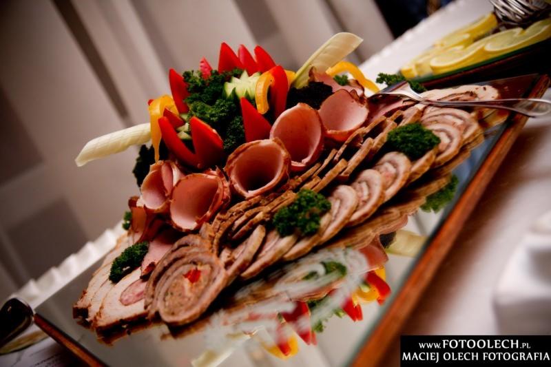 Dekoracyjna kompozycja wędlin, roladek i warzyw (papryka, ogórek, brokuły) na lustrzanej tacy, z cytryną w tle, widoczna refleksja potrawy.