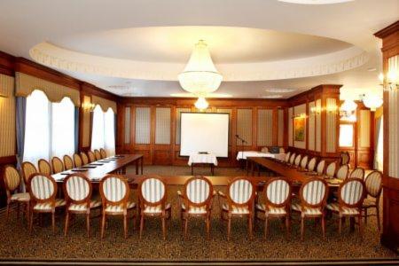 Sala konferencyjna z długimi stołami ustawionymi w podkowę, krzesłami z tapicerką w pionowe pasy, ekranem projekcyjnym i żyrandolem kryształowym.