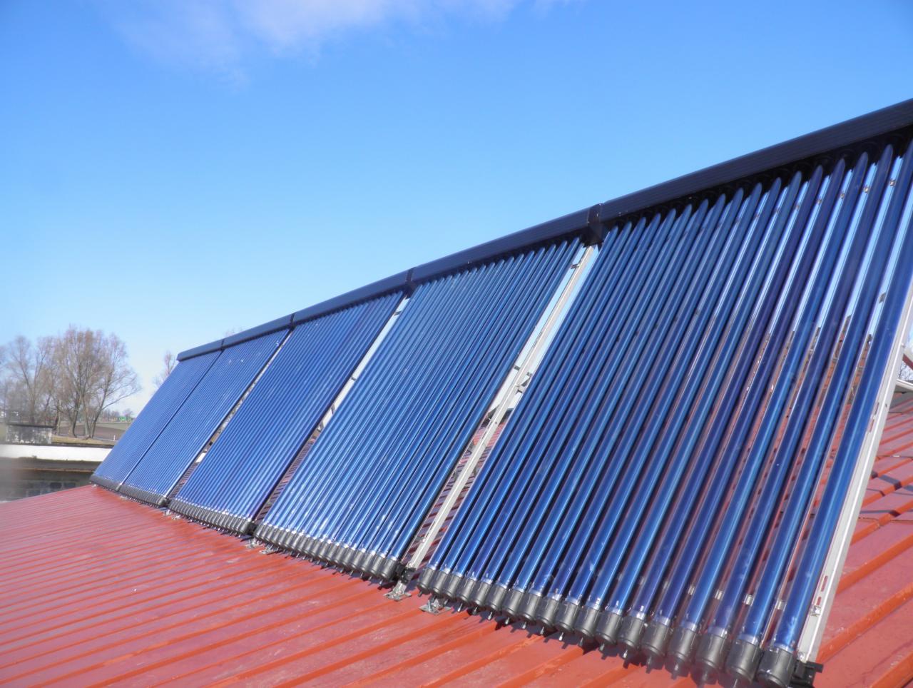 Kolektory słoneczne rurowe zamontowane na dachu z blachy trapezowej w kolorze ceglastym, widoczne na tle błękitnego nieba.