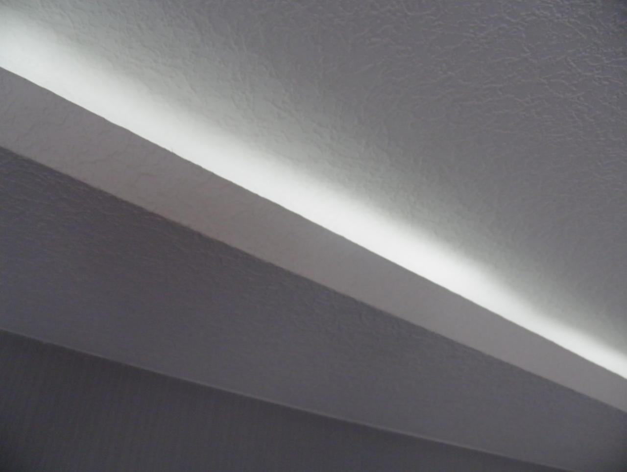 Fragment sufitu z podświetleniem LED, widoczne trzy poziomy sufitu i wąska linia światła LED, oświetlająca górny poziom, struktura powierzchni sufitu imitująca skórę.