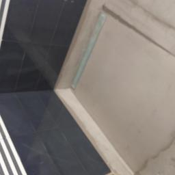 Remonty i wykończenia wnętrz TEAM CONCEPT - Wykończenie łazienki: fragment ściany z surowym tynkiem obok ułożonych, czarno-białych płytek w paski. Widoczny odpływ liniowy.