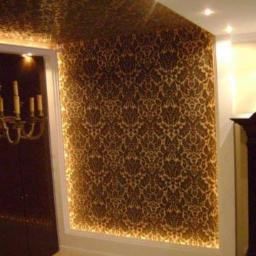 Remonty i wykończenia wnętrz TEAM CONCEPT - Eleganckie wykończenie wnętrza: ściana i sufit pokryte wzorzystą tapetą w odcieniach brązu i złota, subtelne oświetlenie punktowe, dekoracyjny charakter.