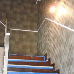 Remonty i wykończenia wnętrz TEAM CONCEPT - Klatka schodowa w trakcie prac wykończeniowych: zabezpieczone taśmą schody, ściany z wzorem w romby, listwy i przewody elektryczne. Etap prac.