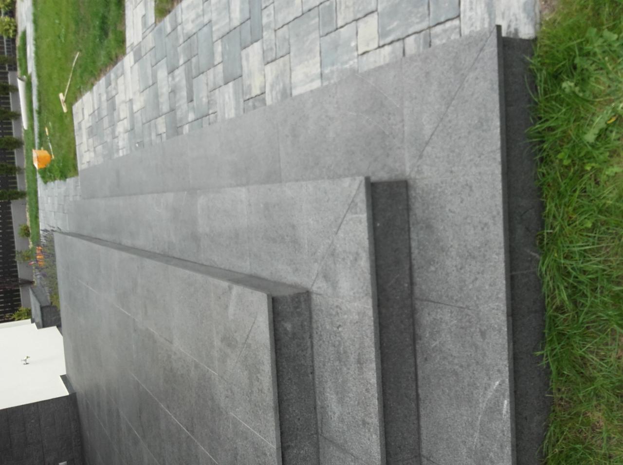 Granitowe schody zewnętrzne prowadzące do kostki brukowej, otoczone trawą. Widok z góry, ukazujący precyzję wykonania i trwałość materiałów.