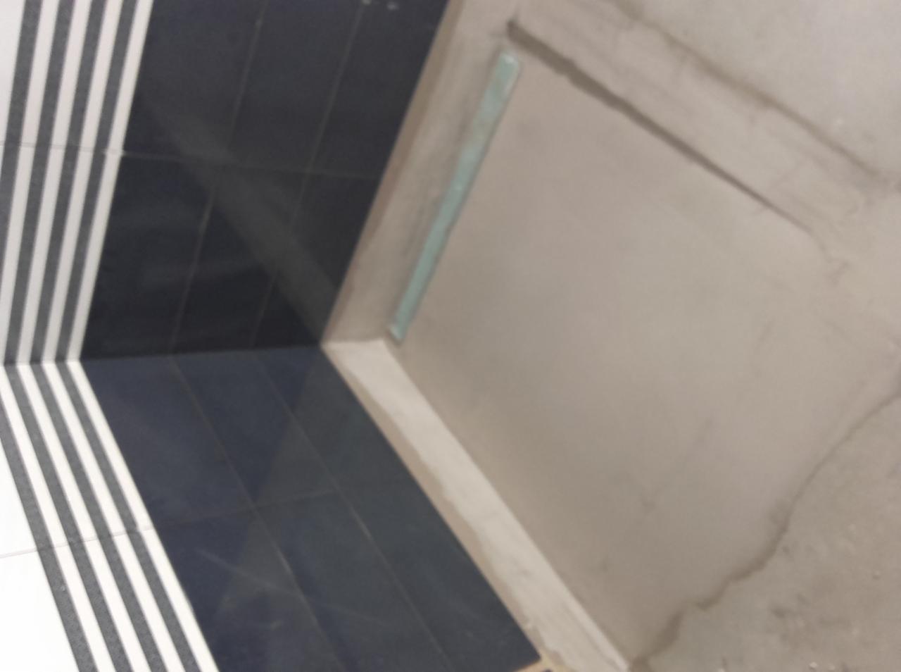 Wykończenie łazienki: fragment ściany z surowym tynkiem obok ułożonych, czarno-białych płytek w paski. Widoczny odpływ liniowy.