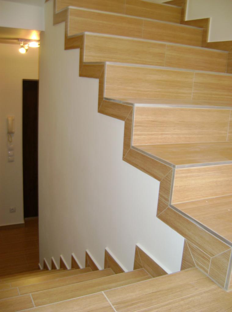 Wykończone schody z płytek imitujących drewno, z widocznymi detalami wykończenia krawędzi i białymi ścianami. Schody prowadzą w głąb jasnego pomieszczenia.