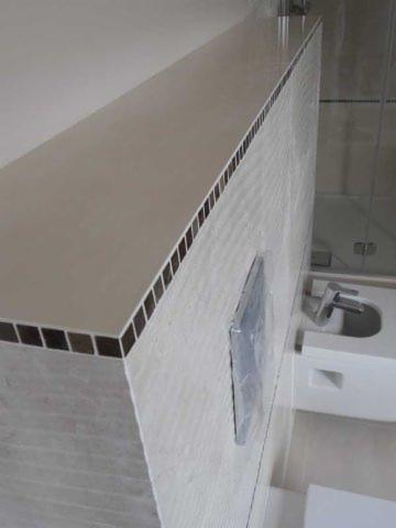 Wykończona łazienka z blatem wyłożonym mozaiką, umywalką i lustrem zabezpieczonym folią. Nowoczesny design w jasnych barwach.