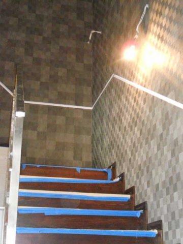 Klatka schodowa w trakcie prac wykończeniowych: zabezpieczone taśmą schody, ściany z wzorem w romby, listwy i przewody elektryczne. Etap prac.