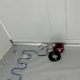 Fragment podłogi z folią aluminiową, na której układane są niebieskie przewody grzewcze, obok leżą zwinięte kable czarne i czerwone, a także składana miarka.