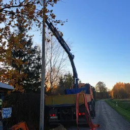 Montaż słupa energetycznego przy użyciu dźwigu samochodowego na tle jesiennego krajobrazu i polnej drogi.