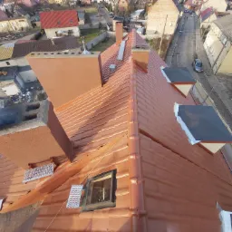 Nowy, miedziany dach z oknem dachowym i zabezpieczeniami kominiarskimi, widok z góry na tle zabudowy miejskiej.