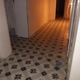 Układanie płytek podłogowych w korytarzu, widoczne fugi i kabel elektryczny na podłodze, ściany przygotowane do malowania.